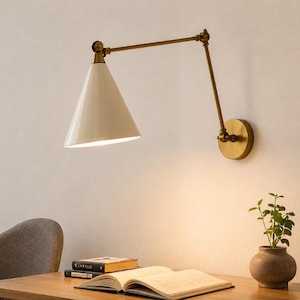 May include: A wall-mounted swing arm lamp featuring a conical off-white shade and a brass-toned metal frame. The fixture has an adjustable arm with visible joints, connecting to a circular wall plate, providing downward light over a desk area.