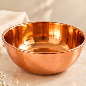 Pode incluir: Uma tigela de mistura em cobre polido com uma superfície lisa e reflexiva e uma borda arredondada. A tigela apresenta uma base circular profunda com um tom laranja-acastanhado metálico quente, exibindo um design limpo e simples.