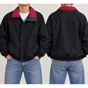 May include: A black windbreaker jacket featuring a contrasting deep red collar and a dark green inner placket detail. The jacket has long sleeves with elastic cuffs, a front snap button closure, and a ribbed hem, shown from front and back views.