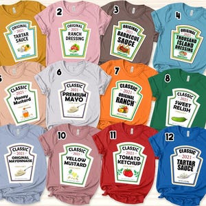 May include: A collection of twelve short-sleeve t-shirts in various colors, each featuring a graphic print of a condiment bottle label. The labels display text such as Tartar Sauce, Ranch Dressing, Barbecue Sauce, Thousand Island, and Tomato Ketchup.