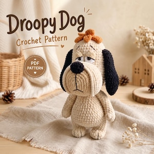 May include: A crocheted dog toy with light beige yarn, long black ears, a dark brown nose, and a small tuft of orange hair on top. The text Droopy Dog Crochet Pattern and a circular badge labeled PDF PATTERN are visible in the background.