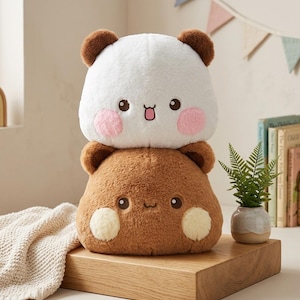 May include: A plush toy featuring two stacked, rounded animal characters. The top character is white with brown ears and pink cheeks. The bottom character is brown with darker brown ears and light yellow cheeks. Both have embroidered faces.