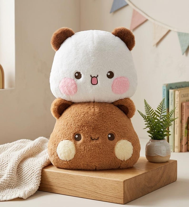 May include: A plush toy featuring two stacked, rounded animal characters. The top character is white with brown ears and pink cheeks. The bottom character is brown with darker brown ears and light yellow cheeks. Both have embroidered faces.