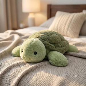 May include: A plush turtle toy with soft, light green fur and a darker green textured shell. The stuffed animal features two small, round black eyes and a simple stitched mouth, resting in a low-profile position with four flippers extended.