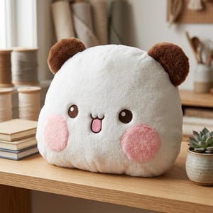 May include: A plush stuffed animal shaped like a rounded creature with white fur, two brown ears, and two pink circular cheeks. The face features embroidered dark brown eyes and a small mouth with a pink tongue sticking out in a playful expression.