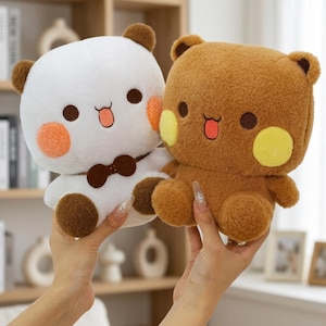 May include: Two plush bear toys, one white with brown ears and a brown bowtie, and one brown with yellow cheeks. Both feature round dark eyes, a small mouth with a pink tongue, and circular cheek patches. The toys have a soft, fuzzy texture.