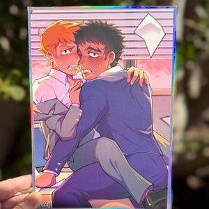 以下が含まれることがあります： スーツを着た二人の人物を描いたアニメスタイルのイラストが特徴の長方形のホログラフィックアートプリント。オレンジ色の髪の人物が座り、暗い髪の人物が抱きしめている。背景にはブラインドとピンク色の空が描かれている。