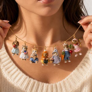 May include: A gold-tone chain necklace featuring seven miniature enamel charms depicting anthropomorphic cats and dogs dressed in various outfits, including a candy corn costume, overalls with vegetables, and dresses with patriotic or floral accents.