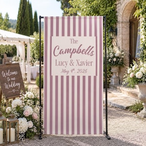 Può includere: Un alto cartello nuziale rettangolare con strisce verticali color malva e bianco. Il centro mostra il testo The Campbells, Lucy & Xavier, e May 4th, 2026, stampato in un carattere malva scuro su un pannello rettangolare bianco solido.