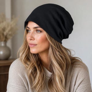Könnte beinhalten: Eine einfarbige, schwarze Slouch-Beanie aus weichem, glattem Stoff. Die Mütze hat eine abgerundete Krone und eine lockere Passform, die bequem auf dem Kopf sitzt und eine vollständige Abdeckung mit einem schlichten, klaren Design ohne Muster bietet.
