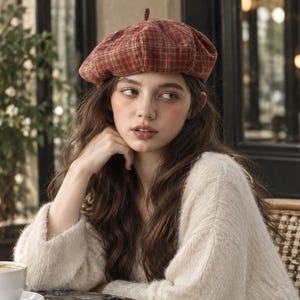 Puede incluir: Una boina de cuadros rojos y marrones que presenta una pequeña lengüeta de tela en la parte superior central. El gorro está confeccionado con un tejido suave y texturizado, con una forma redondeada clásica y una corona estructurada.