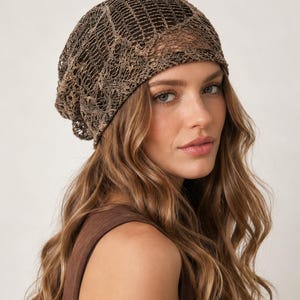 May include: A slouchy beanie hat crafted from a dark brown, open-knit fabric with a metallic gold thread woven throughout. The hat features a loose, textured weave pattern that creates a semi-sheer appearance, providing a relaxed fit.