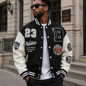 May include: A black and white varsity jacket featuring the number 23, a large letter B, and various basketball-themed patches. The jacket has white sleeves, a black body, a snap-button front, and striped ribbed cuffs and collar.