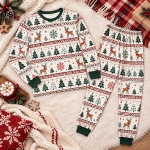 May include: A two-piece pajama set featuring a long-sleeved crew neck top and matching pants. The fabric is white with a repeating holiday pattern of green pine trees, red snowflakes, and brown reindeer wearing red scarves, finished with dark green cuffs.