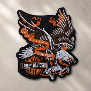 May include: A black embroidered patch featuring a large eagle with brown and white feathers. An orange banner across the eagle reads RIDE FREE in white text. Below, an orange and black Harley-Davidson Motor Clothes logo is prominently displayed.