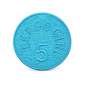 May include: A circular, bright cyan embroidered patch featuring a stitched border. The text "LET GO GIRL" is arched across the top half, and the number "5" is prominently centred in the middle of the patch in a matching cyan thread.