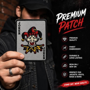 May include: A rectangular embroidered patch featuring a gray background with a central joker character wearing a red and black jester hat and collar. The word JOKER is printed vertically in black along the left and right edges of the patch border.