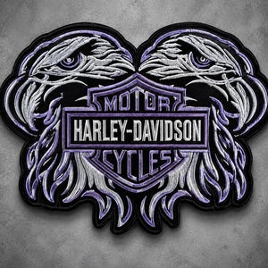 May include: A large embroidered patch featuring two eagle heads facing outward in shades of purple, white, and black. Centered between the eagles is a purple and white shield emblem with the text MOTOR HARLEY-DAVIDSON CYCLES in white lettering.