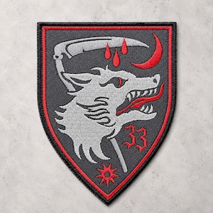 May include: A shield-shaped embroidered patch with a black background and a red border. It features a grey wolf head in profile, a grey scythe, three red blood drops, a red crescent moon, the red number 33, and a red star-like symbol at the base.