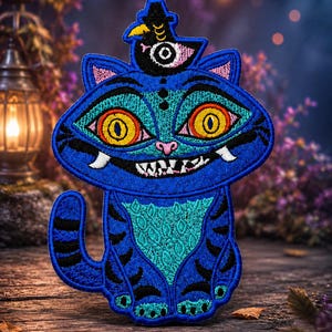 Puede incluir: Un parche bordado que muestra un gato azul brillante con grandes ojos amarillos, una amplia sonrisa y rayas negras. Un pequeño pájaro negro con sombrero de copa está sobre la cabeza del gato. El diseño utiliza hilo azul, turquesa, amarillo y negro.