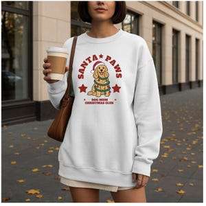 May include: A white long-sleeve sweatshirt featuring a graphic of a golden dog wearing a Santa hat and wrapped in Christmas lights. The text reads SANTA PAWS and DOG MUM CHRISTMAS CLUB in red lettering, accented by two red stars on the sides.