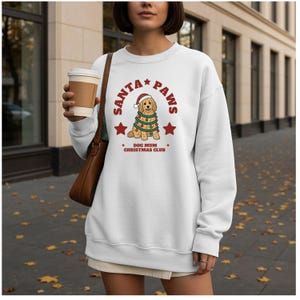 May include: A white long-sleeve crewneck sweatshirt featuring a graphic of a golden-colored dog wearing a Santa hat and wrapped in Christmas lights. The text reads SANTA PAWS and DOG MUM CHRISTMAS CLUB in red lettering with two red stars.
