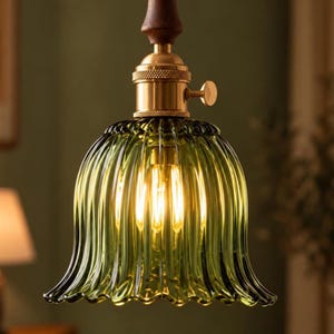 May include: A pendant light fitting featuring a bell-shaped, ribbed olive green glass shade. The top of the shade is secured by a polished brass socket with a small side turn knob, connected to a dark brown wooden cylindrical ceiling mount.