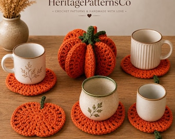 May include: A set of orange crochet pumpkin coasters and a central crochet pumpkin decoration. The coasters are round with a small green stem, and the mugs are ceramic with botanical prints. The text HeritagePatternsCo is visible above.