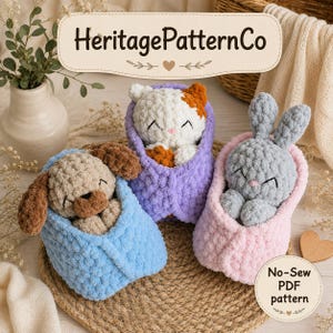 May include: Three crocheted plush animals wrapped in blankets: a brown dog in a light blue blanket, a white and orange cat in a purple blanket, and a gray rabbit in a pink blanket. The image includes the text HeritagePatternCo and No-Sew PDF pattern.