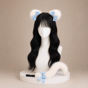 May include: A set of white faux fur animal ears on a headband, each adorned with a light blue satin bow, paired with a matching white faux fur tail featuring a light blue satin bow and a black adjustable strap with a metal buckle.
