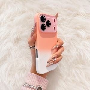 May include: A smartphone case featuring a smooth gradient design that transitions from a soft peach-orange at the top to a solid white at the bottom. The case includes a raised, matching peach-colored camera lens protector frame with three circular cutouts.