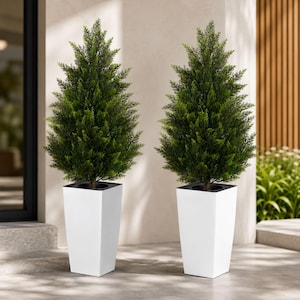 May include: Two artificial cone-shaped evergreen trees with dense green foliage, each planted in a tall, tapered, matte white square planter. The plants feature realistic needle-like leaves and are positioned upright on a flat surface.