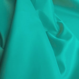 May include: A close-up of a smooth, teal fabric with soft folds and wrinkles.