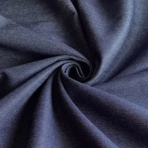 May include: Close-up of a dark blue denim fabric with a textured weave. The fabric is folded and draped, showing its soft and pliable texture.