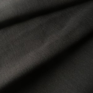 May include: Close-up of a black fabric with a subtle ribbed texture. The fabric is folded and draped, creating soft folds and shadows.