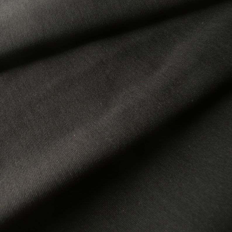May include: Close-up of a black fabric with a subtle ribbed texture. The fabric is folded and draped, creating soft folds and shadows.