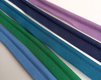 May include: Five different colours of bias binding, including light blue, teal, green, navy blue, and purple. The binding is folded and sewn with a straight stitch.