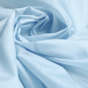 May include: A close-up shot of light blue fabric, showing soft folds and a swirling design. The material has a smooth appearance and a gentle sheen, giving a sense of depth and texture. The overall effect is elegant and delicate.