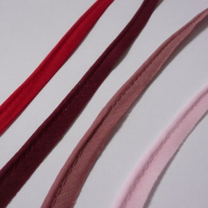 May include: Four different colours of bias tape, from red to pink, with a white background.