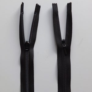 May include: Two black zipper pulls with a black zipper tape. The zipper pulls are open and the zipper tape is closed.