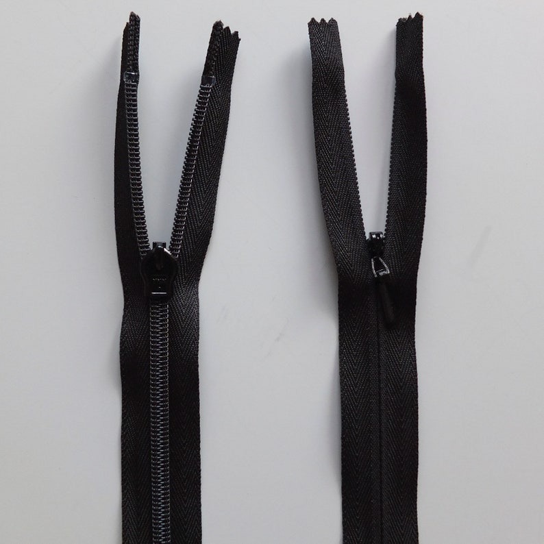 May include: Two black zipper pulls with a black zipper tape. The zipper pulls are open and the zipper tape is closed.