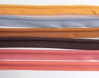 May include: Five different coloured fabric trims with a stitched edge. The trims are arranged in a stack from top to bottom: orange, grey, brown, pink, and coral.