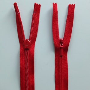 May include: Two red zippers with metal sliders. The zippers are open and the sliders are in the middle of the zipper.