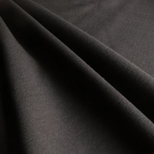 May include: Close-up of a black fabric with a subtle texture. The fabric is folded and draped, creating soft folds and shadows.