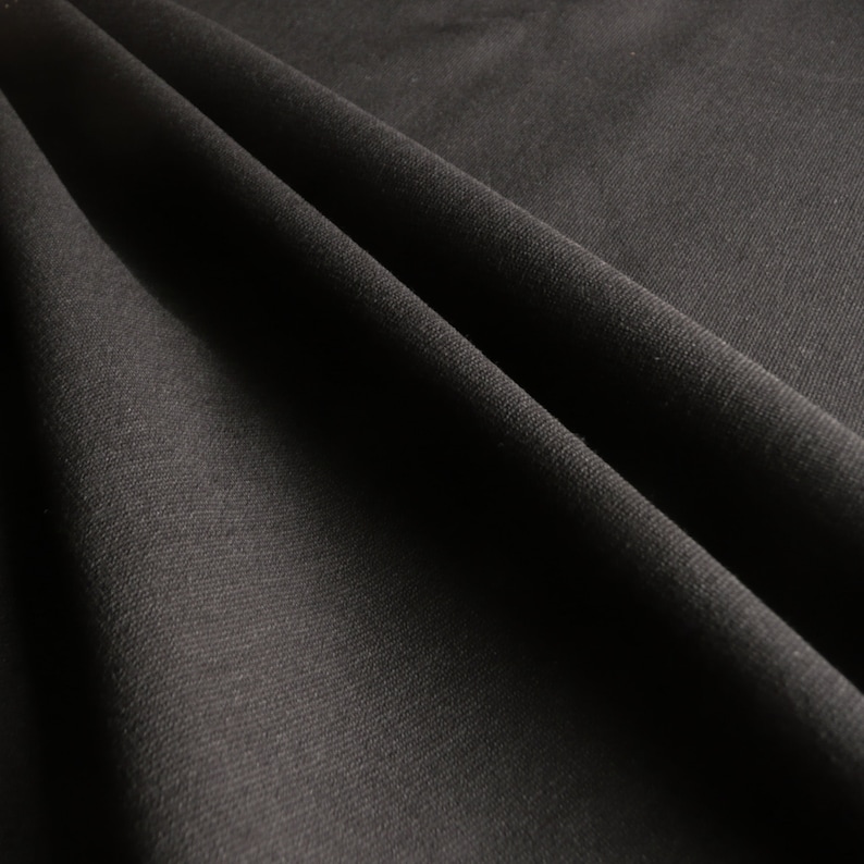 May include: Close-up of a black fabric with a subtle texture. The fabric is folded and draped, creating soft folds and shadows.