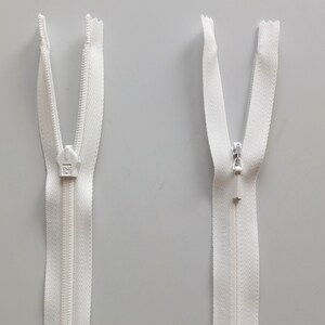 May include: Two white zipper pulls with a white zipper tape. The zipper pulls are open and the zipper tape is visible.