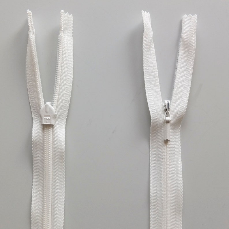 May include: Two white zipper pulls with a white zipper tape. The zipper pulls are open and the zipper tape is visible.