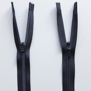 May include: Two black zipper pulls with metal sliders. The zippers are open and the teeth are visible.