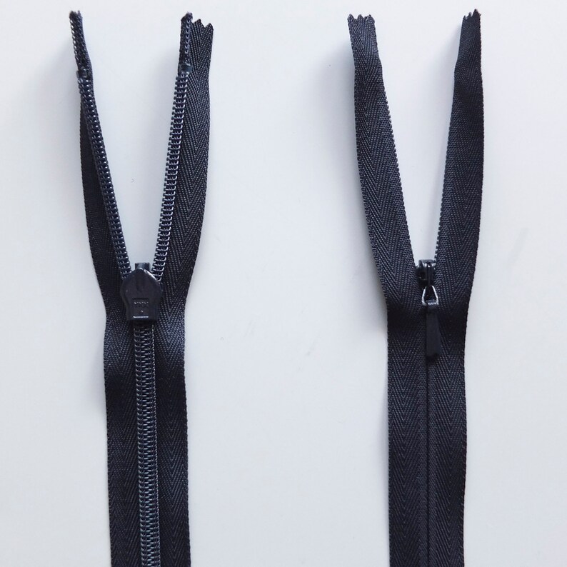 May include: Two black zipper pulls with metal sliders. The zippers are open and the teeth are visible.