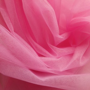 May include: Pink tulle fabric with a soft, delicate texture. The fabric is gathered and draped, creating a flowing and airy look.